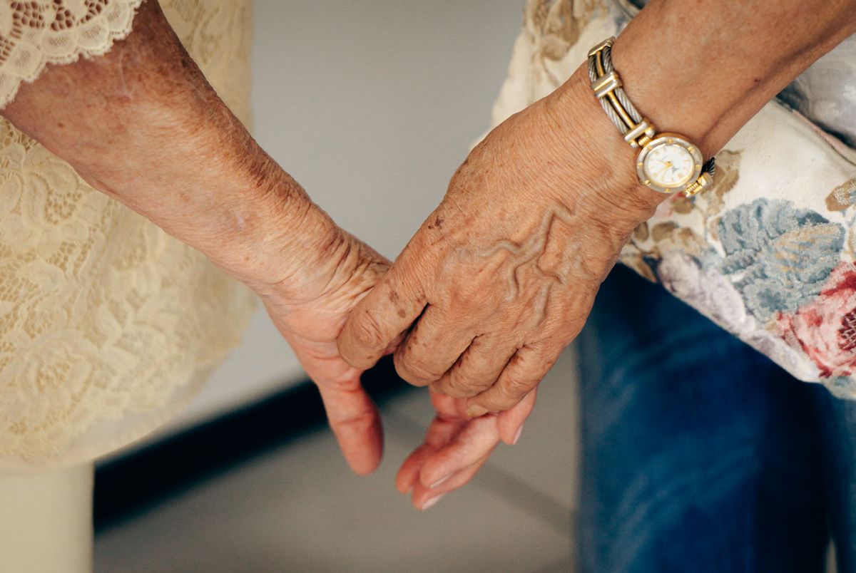 Two women's hands clasped, the older one wearing a gold wristwatch.